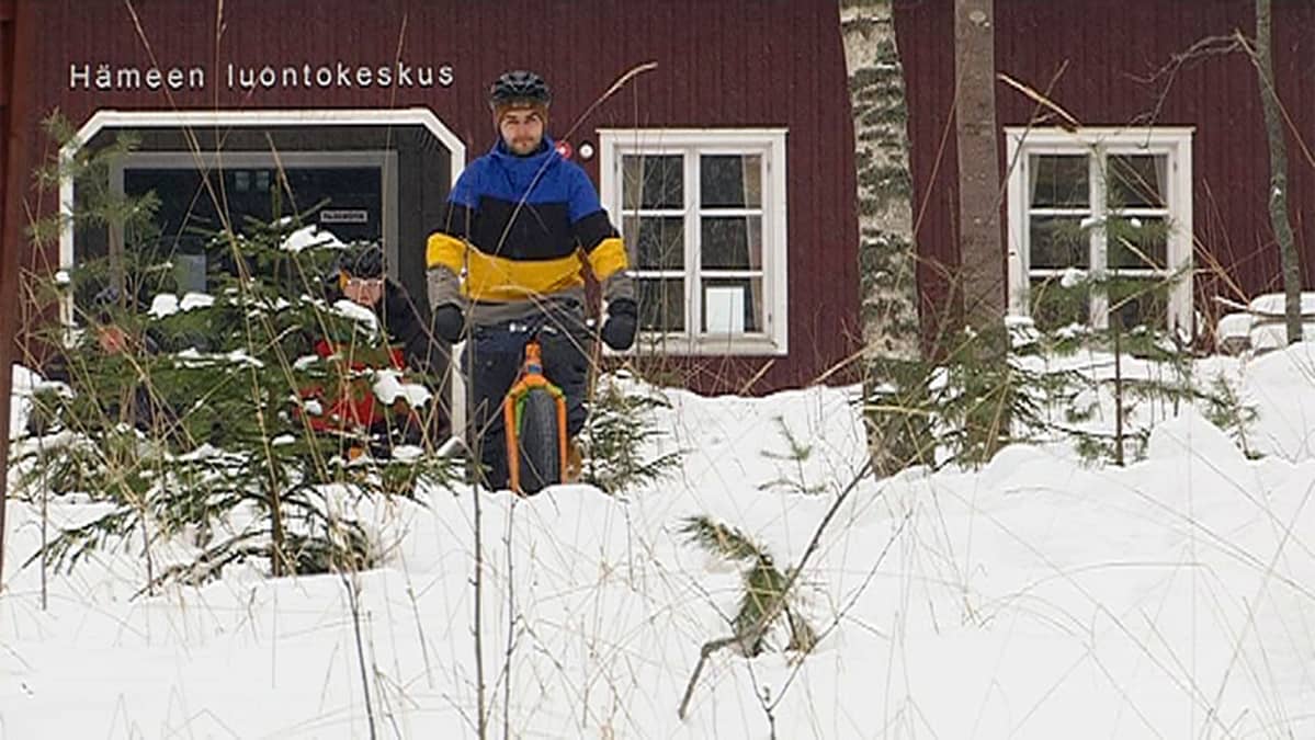 Mies pyöräilee fatbikella talvisessa maastossa takanaan Hämeen luontokeskus