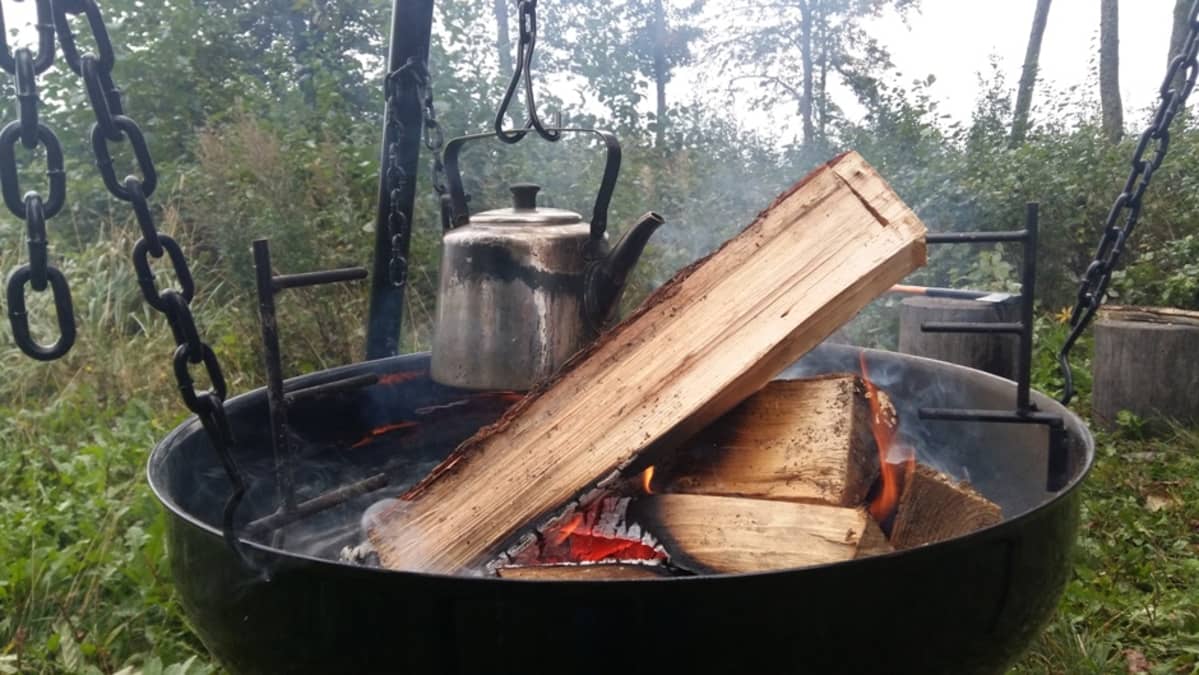 Kahvipannu telineessä nuotiolla. Puita.