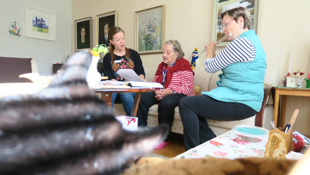 Sairaalamuusikko Iida-Maria Uljas ja lähihoitaja Sari Perätalo kotihoidon käynnillä Aune Kuusenhakon luona.
