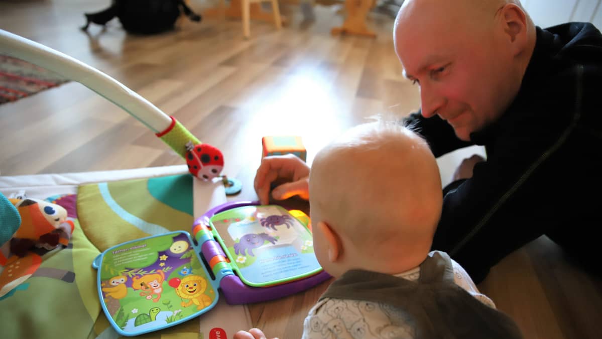 Juho Vesalainen lukee kirjaa Otso-vauvalle lattialla.