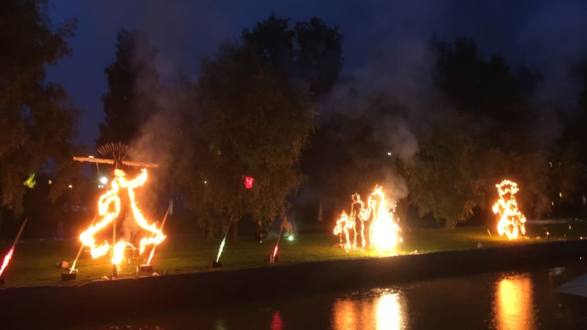 Kuvassa valoesityksen tulihahmoja veden äärellä
