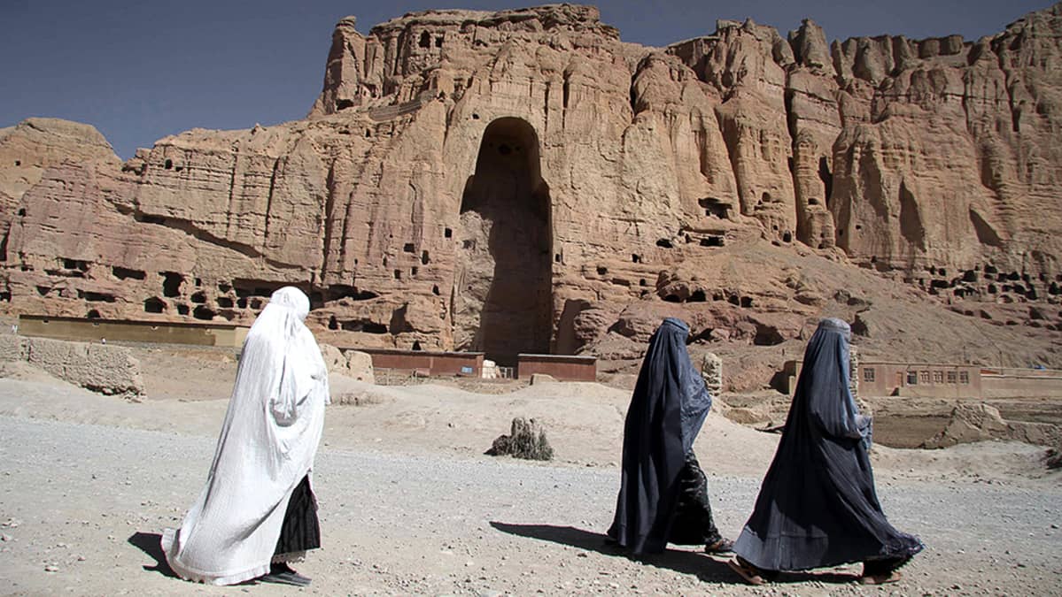 Afgaaninaiset kävelevät Bamianin laaksossa toisen talibanien tuhoaman buddha-patsaan paikan ohitse.