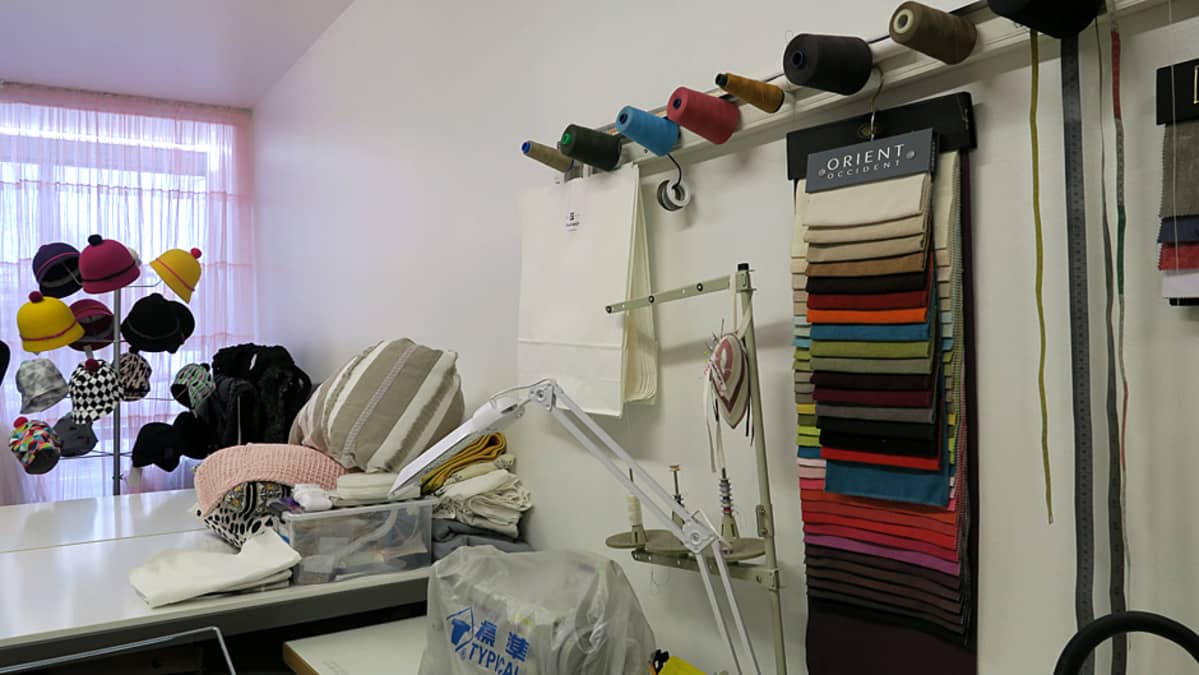 Hattuja telineessä ja kangasmallitilkkuja seinällä