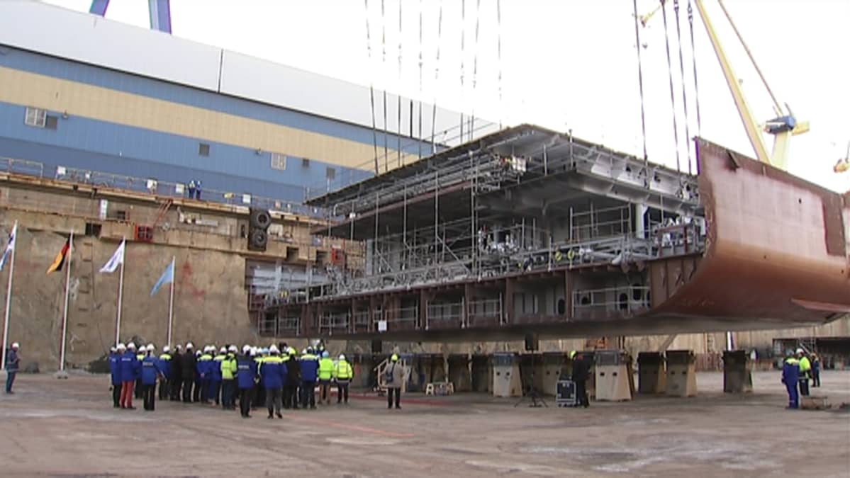 Ihmiset seuraavat matkustaja-aluksen kölinlaskua Turun telakan rakennusaltaassa.