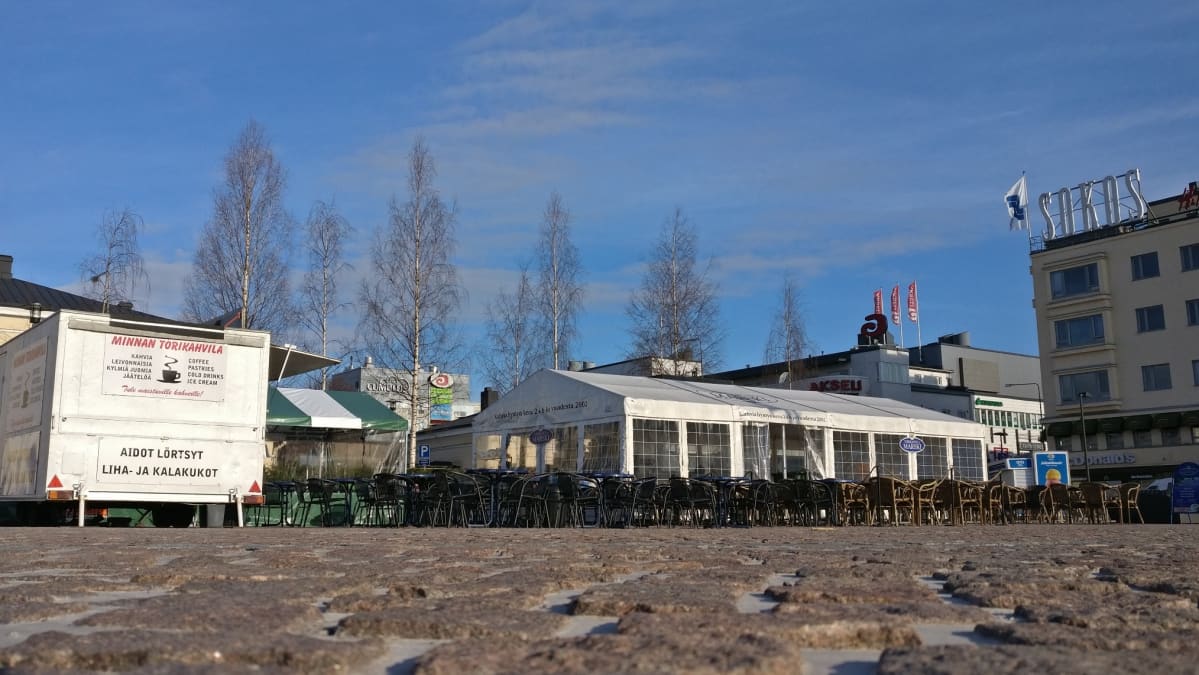 Kuva Mikkelin torilta. Kuvassa torikahvila ja toisen torikahvilan myyntikärri. Taivas on sininen ja ympäristön puut ovat vielä lehdettömiä.