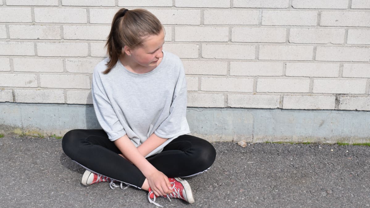 nuori tyttö istuu ulkona nojaten tiiliseinään