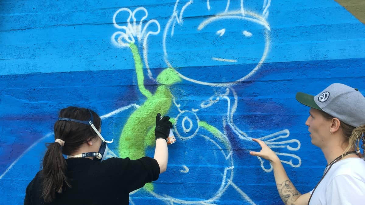 Kouvolalainen Tirliina Parviainen maalaa sammakkokuvan pohjaväriä graffitikouluttaja Emilio Mäkipään opastuksessa