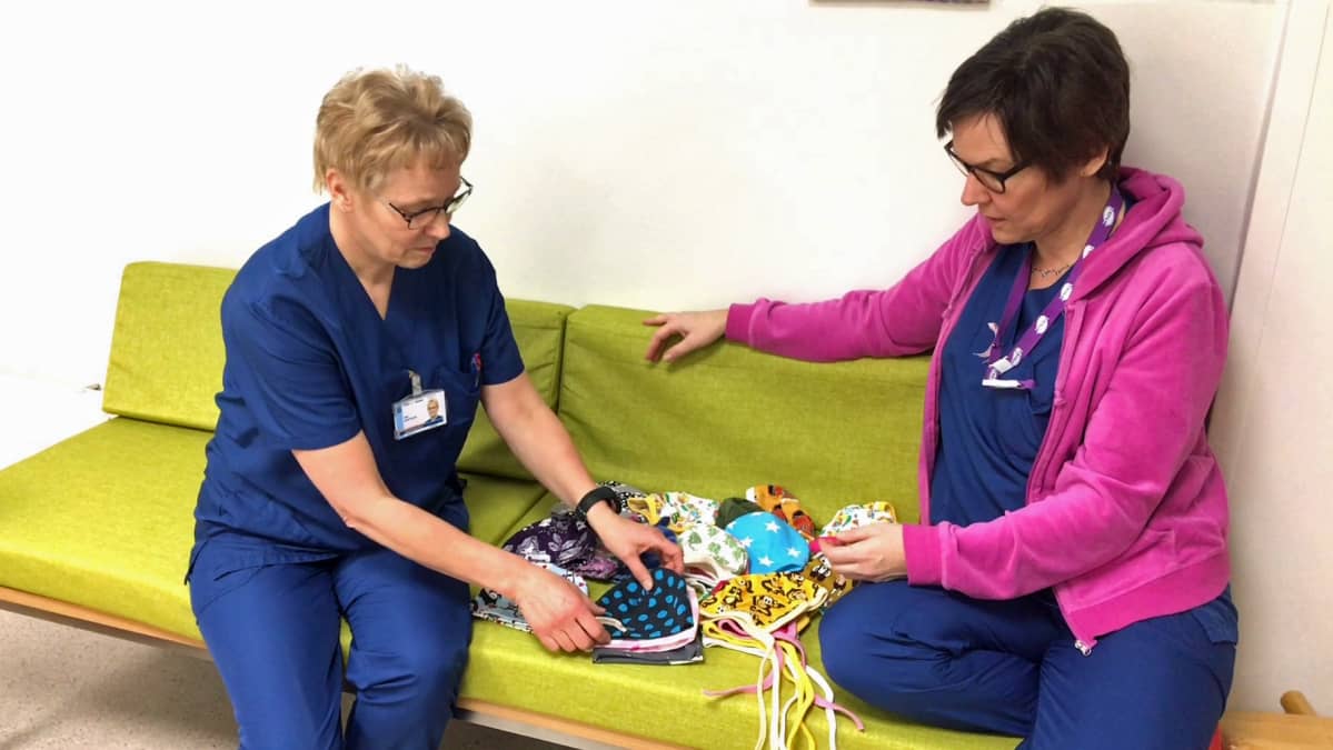 Osastonhoitaja Tiina Kemppainen ja kätilö Mary Viander-Laine katsovat pipoja sohvalla