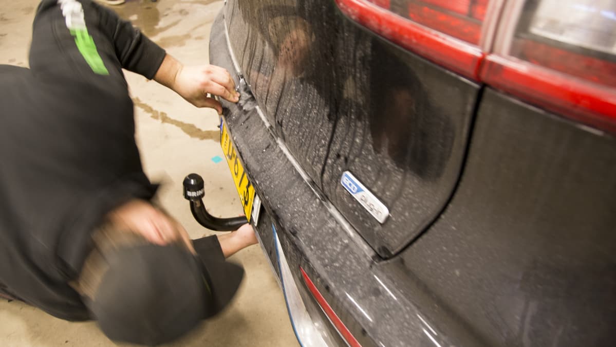 Koukkupajan asentaja asentaa vetokoukkua hybridiautoon.