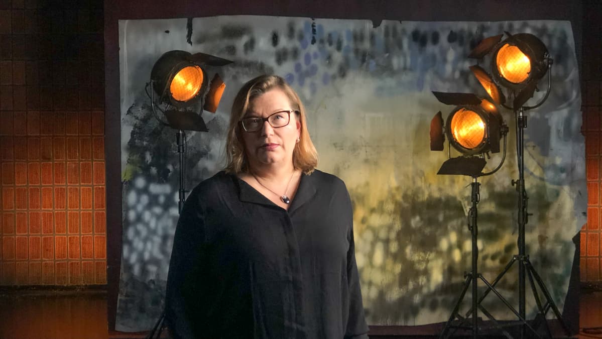 Kaisa rastimo seisoo studiossa taustalavasteen ja studiolamppujen edessä. Kuva otettu lyhytvideosarjaan Me elokuvantekijät.