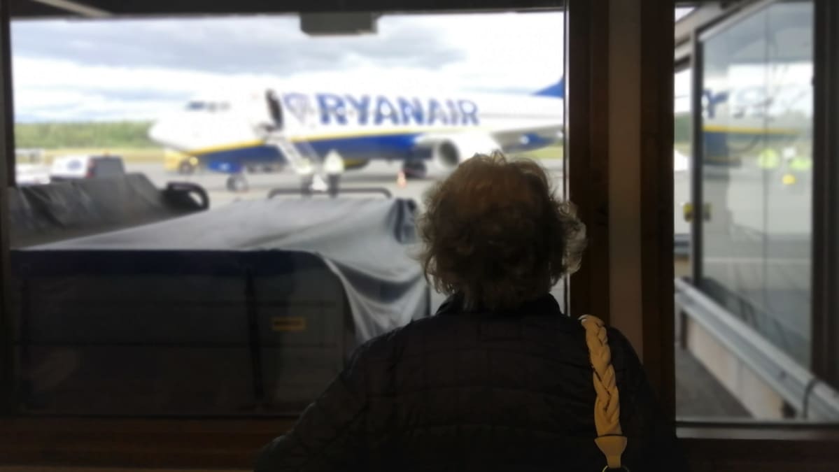 Iäkäs nainen seuraa ikkunasta Ryanairin koneen laskeutumista