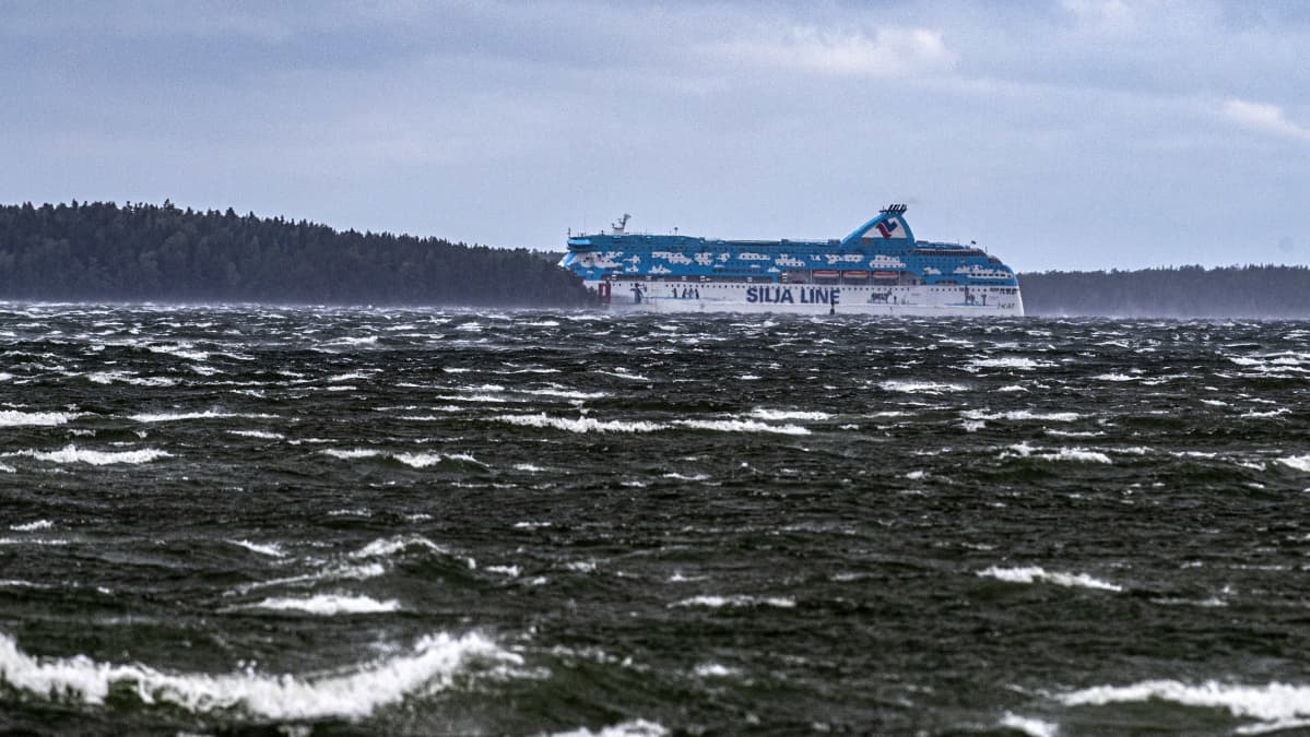 Tallink Siljas blåvita passagerarfartyg Galaxy försvinner bakom en ö under en höststorm med vita toppar på vågorna.