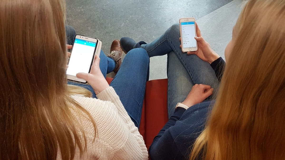 kaksi yläkoululaista katsoo kännyykkäänsä