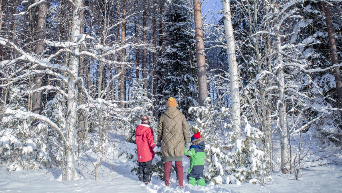 Äiti ja kaksi lasta seisovat metsän reunassa