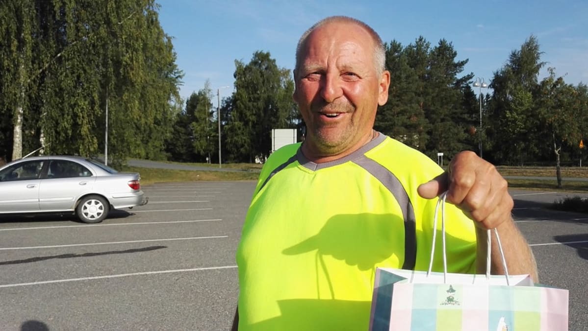 Mies myhäilevänä muumimukikassi kädessään