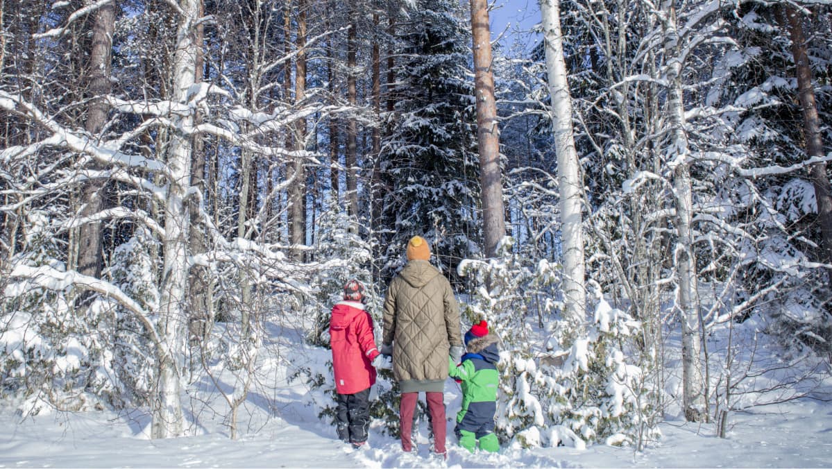 Äiti ja kaksi lasta seisovat metsän reunassa