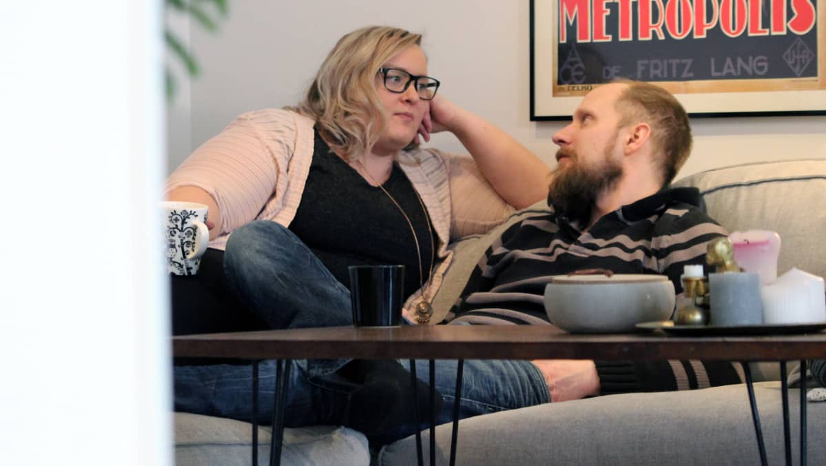 Tanja Rongas ja Tomppa Ojava keskustelemassa olohuoneensa sohvalla kahvikuppien äärellä