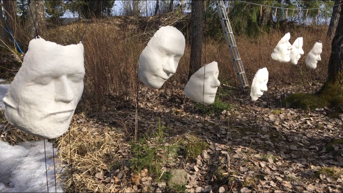 Valkoisia naamioita vaijerissa puiden välissä järven rannalla.