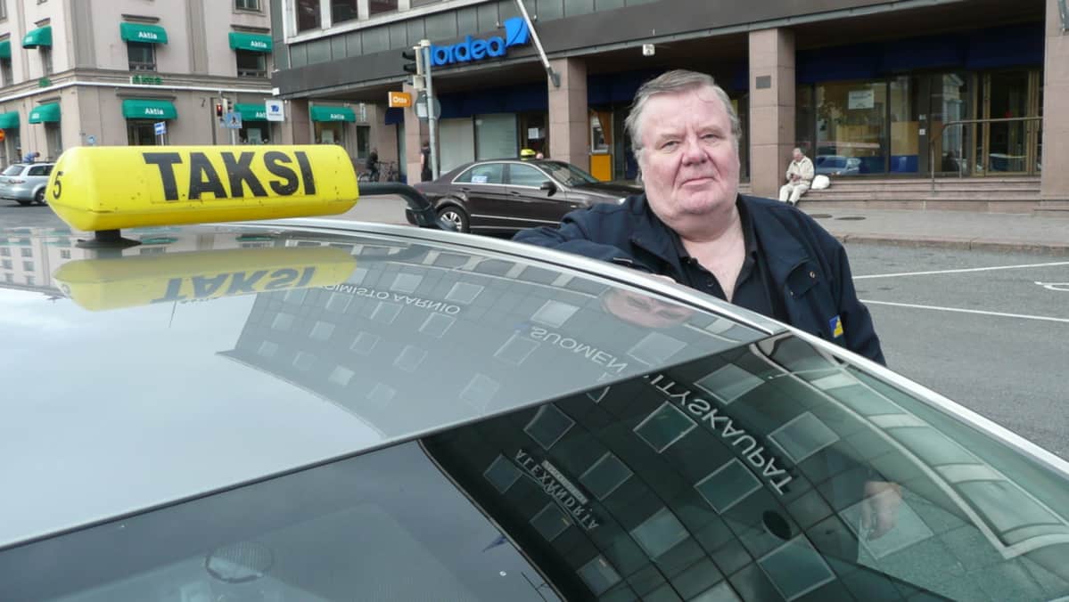 Taksinkuljettaja nojaa autoonsa.