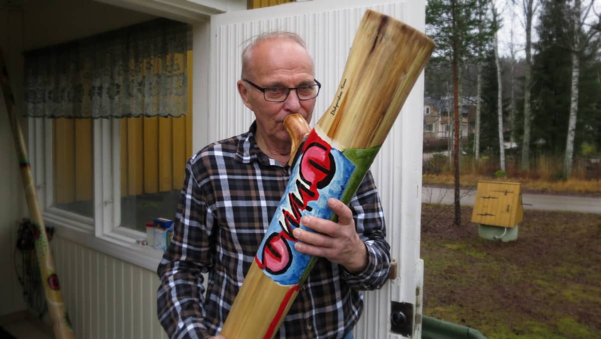 Mies puhaltaa kotitalon portailla puiseen soittimeen