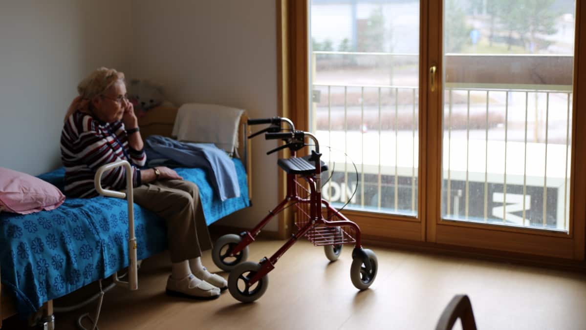 Ikääntynyt nainen istuu sängyllään ja puhuu kännykkään.