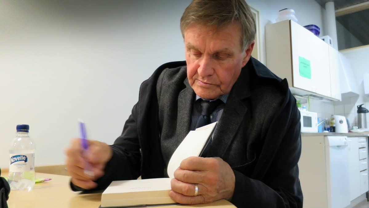 Mies kirjoittaa kirjan sisälehdelle omistuskirjoitusta