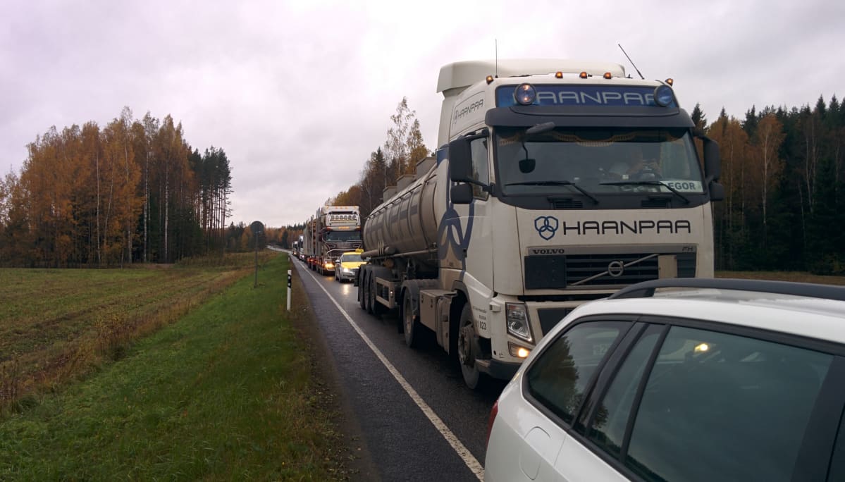 Kuorma-autoja ja henkilöautoja jonossa maantiellä.