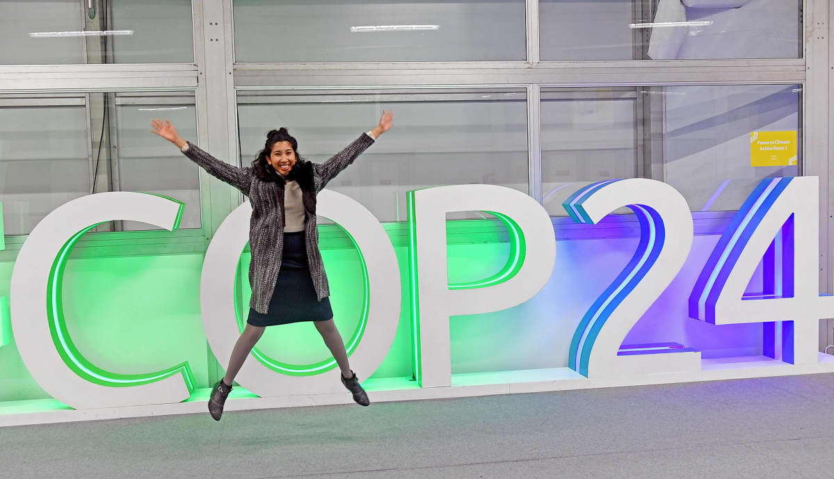 Nainen poseeraa COP24-kyltin edessä.