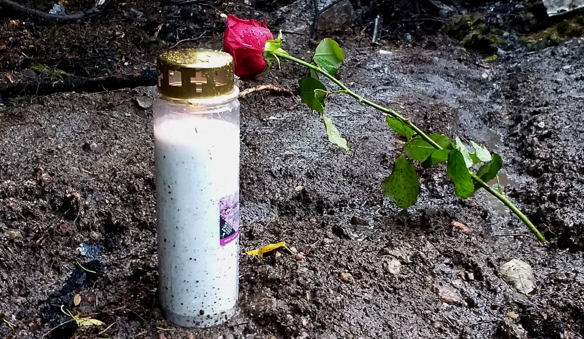 Muistokynttilä ja punainen ruusu maassa.