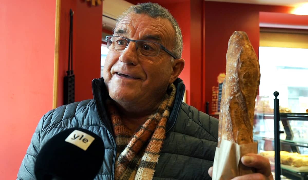 Vanhempi silmälasipäinen herrasmies Gérard seisoo leipomossa patonki kädessä. Etualalla näkyy Ylen mikrofoni.