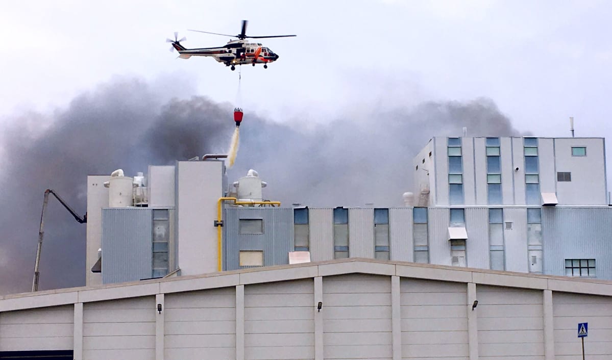 Rajavartiolaitoksen helikopteri tiputtaa vettä tehtaaseen.