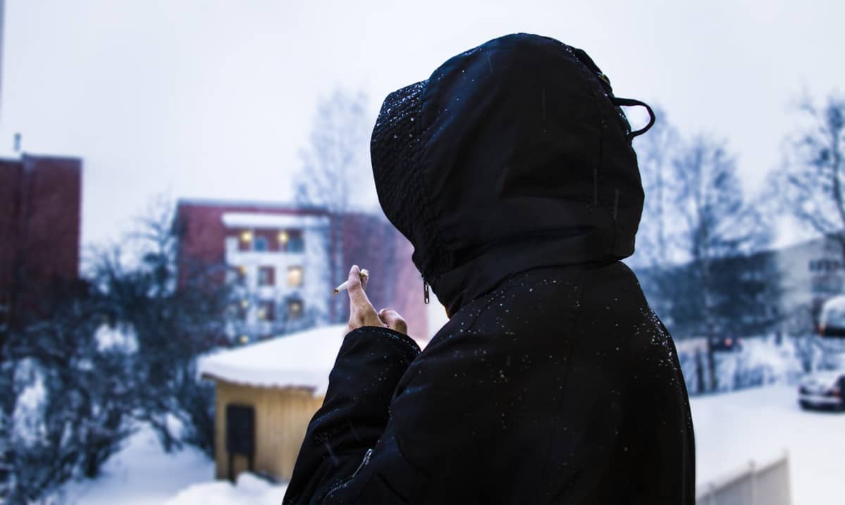 Anonyymi nainen seisoo parvekkeella ja polttaa tupakkaa