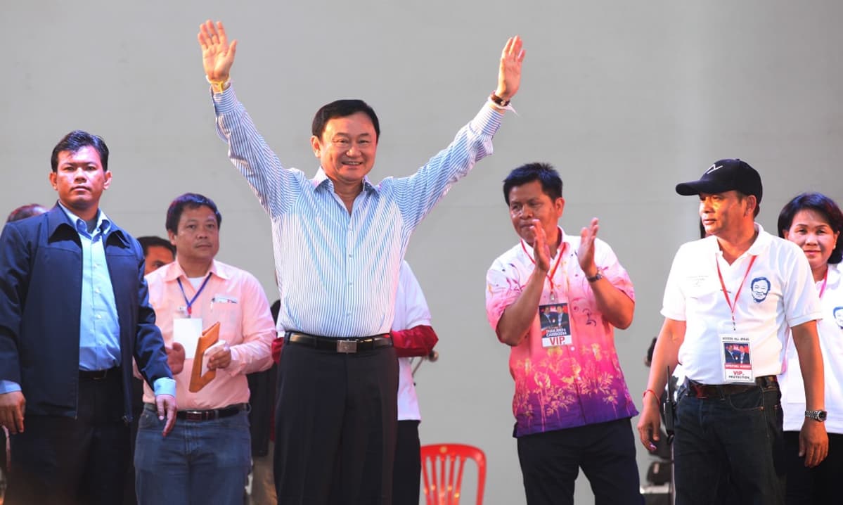 Thaksin Shinawatra tuulettaa kädet pystyssä lavalla. Hänen taustallaan on useita ihmisiä.
