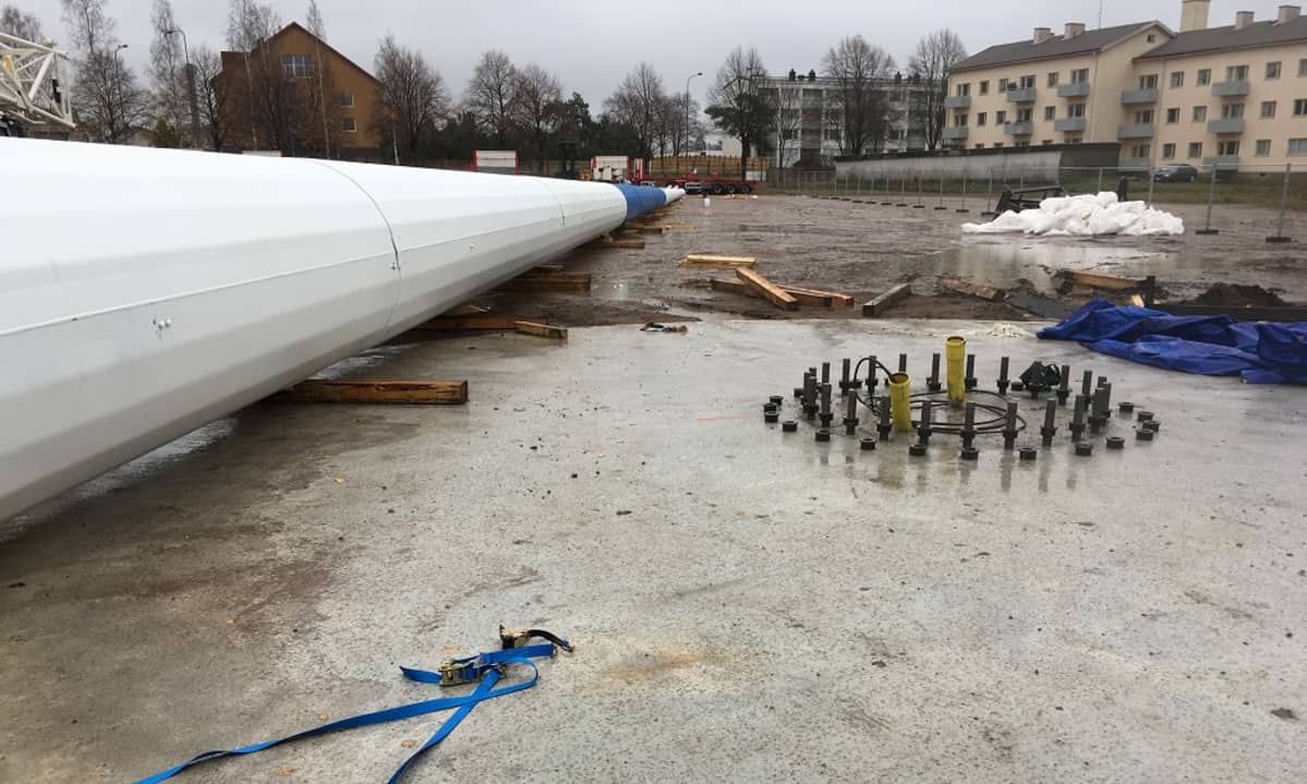 Sinivalkoinen lipputanko pitkin pituuttaan hiekkakentällä, vieressä pultit, joihin tanko on tarkoitus kiinnittää.