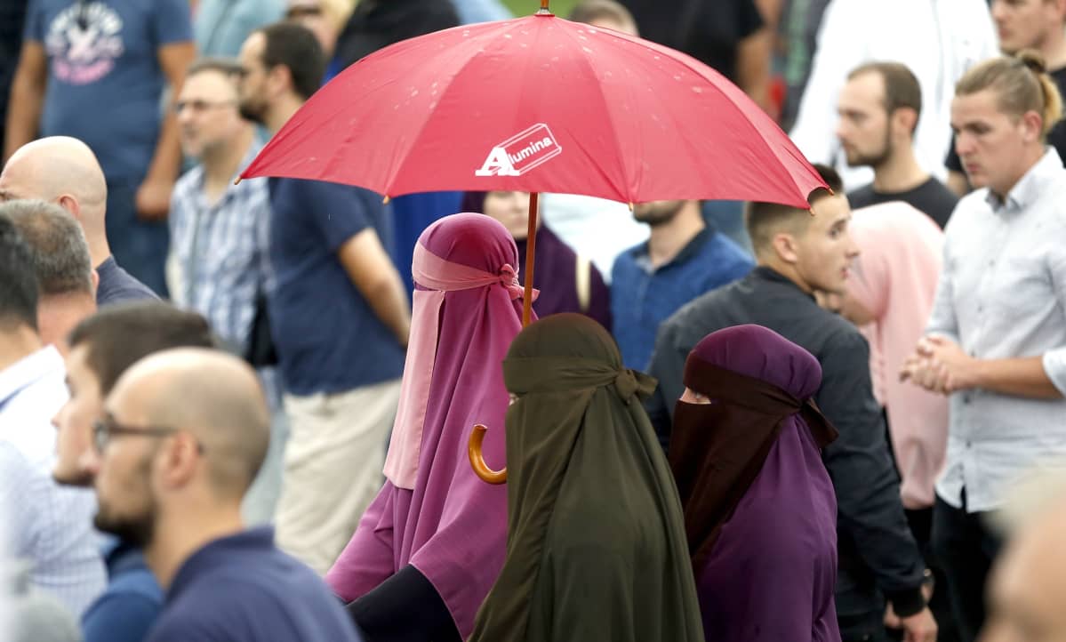Kolme peittäviin kaapuihin pukeutunutta musliminaista ja joukko muita mielenosoittajia.