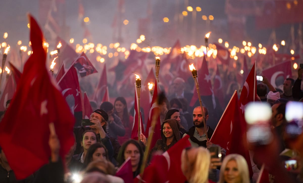 Tuhannet ihmiset polttavat soihtuja ja kantavat Turkin lippuja iltahämärässä.