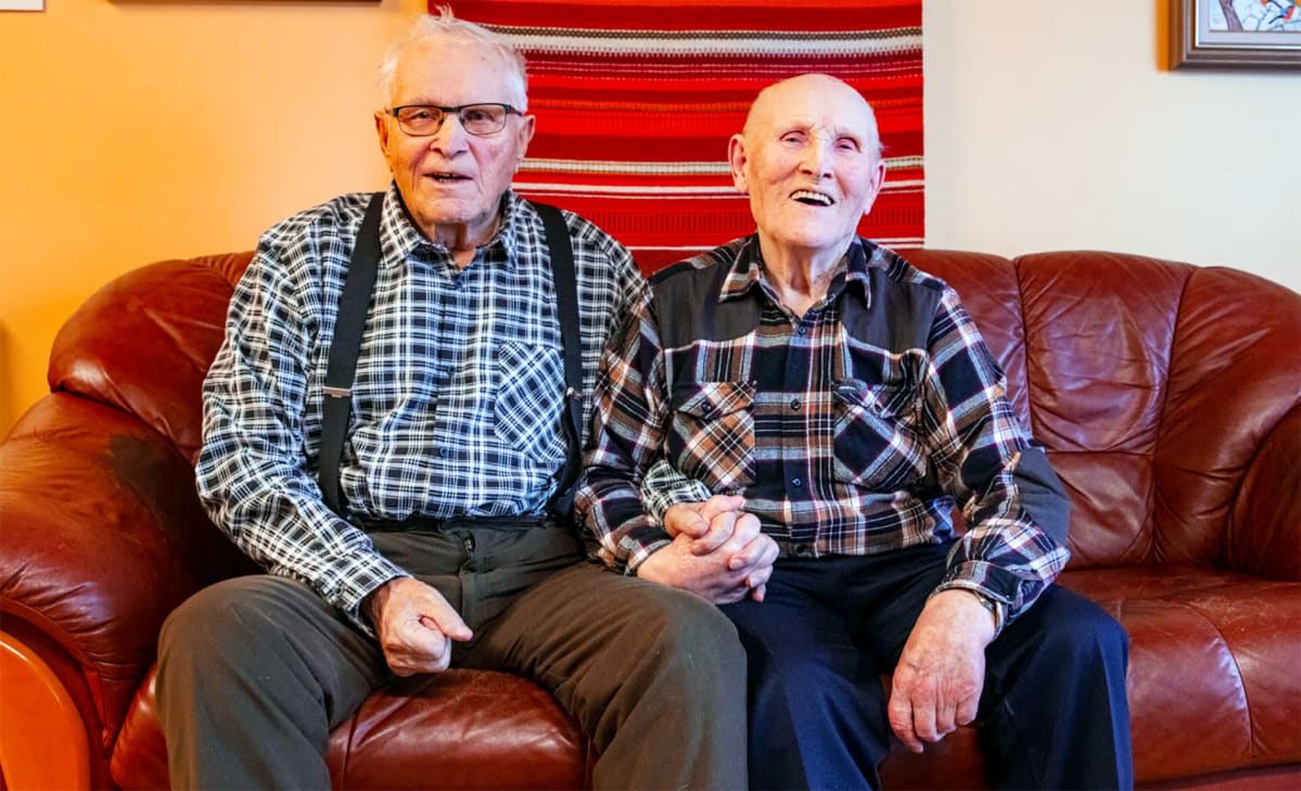 Eino ja Väinö kinnunen istuvat sohvalla ja pitävät käsiä.