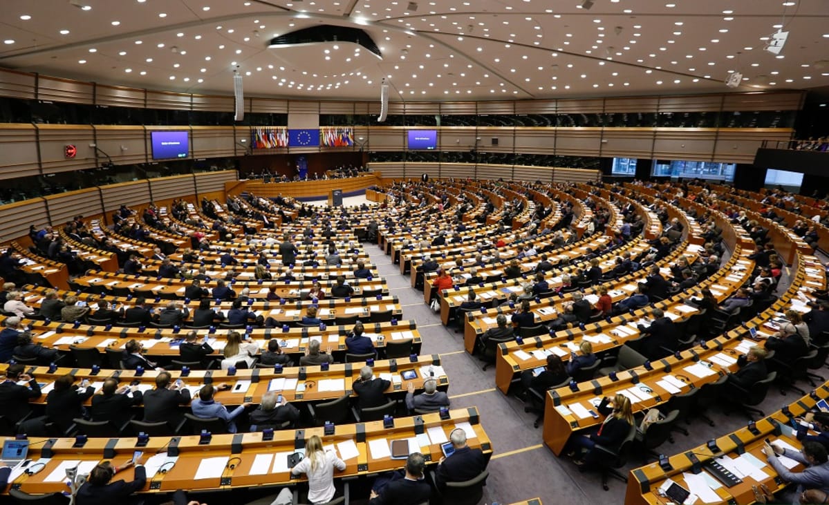 Kuva Euroopan parlamentin istuntosalista, jossa edustajien pöydät levittäytyvät puheenjohtajan korokkeesta. Puheenjohtajan korokkeen yllä on EU:n lippu ja jäsenvaltioiden liput.