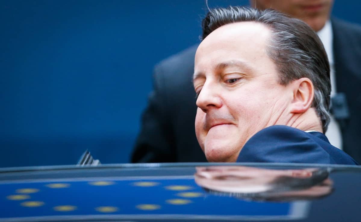 Britannian pääministeri David Cameron on istuutumassa autoon. Cameronista näkyvät auton takaa pää ja vasen olkapää. Hänellä on sininen puku. Cameronilla on kasvoillaan hieman vaikea ilme, autoon ahtautuminen on hieman hankalaa. Auton kattoon heijastuvat jostain EU:n sinisen lipun keltaiset tähdet. Taustalla seisoo mies tummassa puvussa, mahdollisesti turvamies. Tausta on tummansininen.