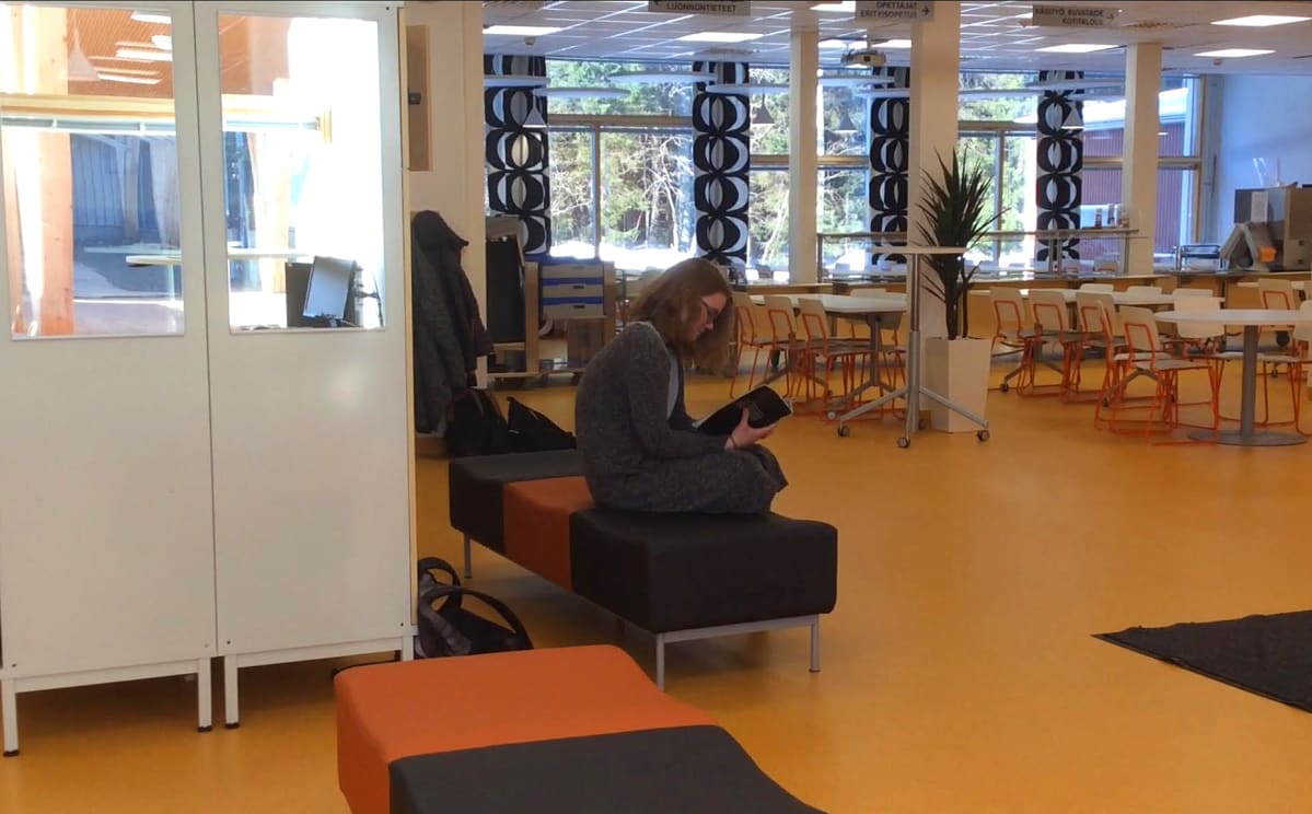 Oppilas lukee kirjaa koulun aulassa.
