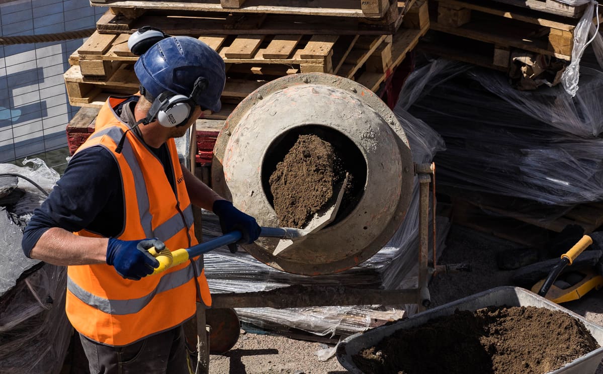 Rakennustyöläinen lapioi hiekkaa betonimyllyyn.