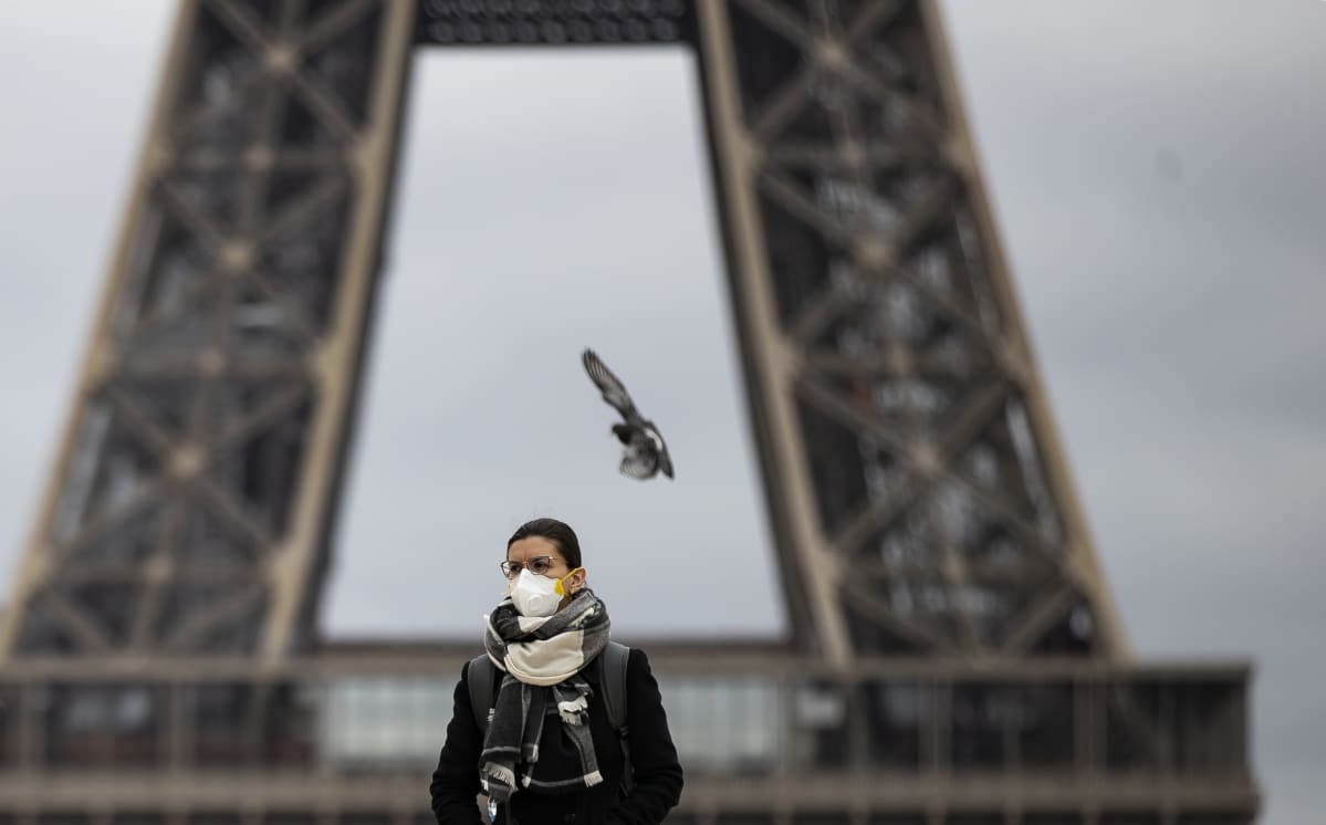 Hengityssuojaan pukeutunut nainen seisoo Eiffel-tornin edessä.