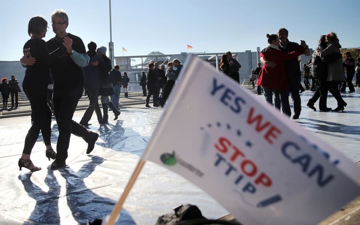 Pareja tanssimassa tangoa TTIP:n vastaisen lipun takana.