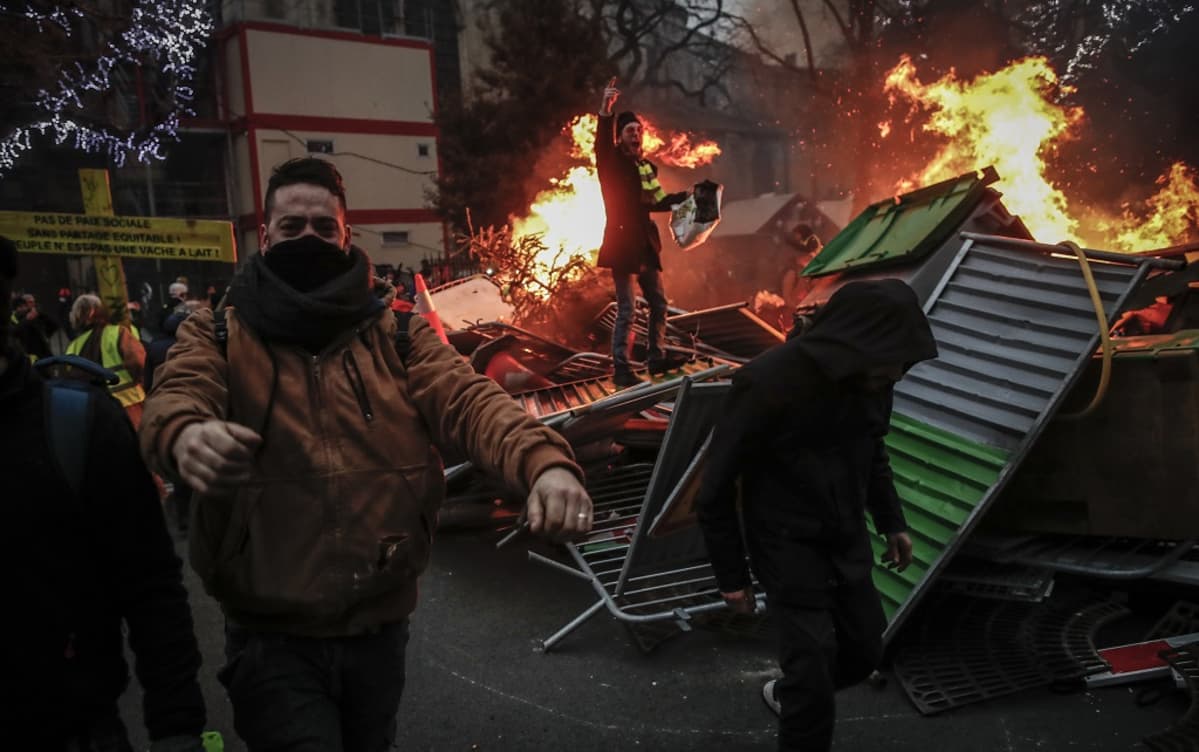 Kasvonsa peittäneitä mielenosoittajia heiluu palavien barrikadien luona.
