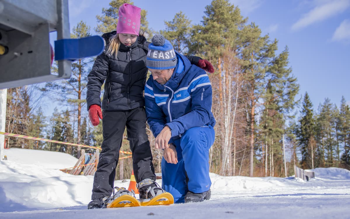 Pohjois-tiipaksen koulun johtaja, Ilkka Korhonen, auttaa oppilaalle lumikenkiä jalkaan