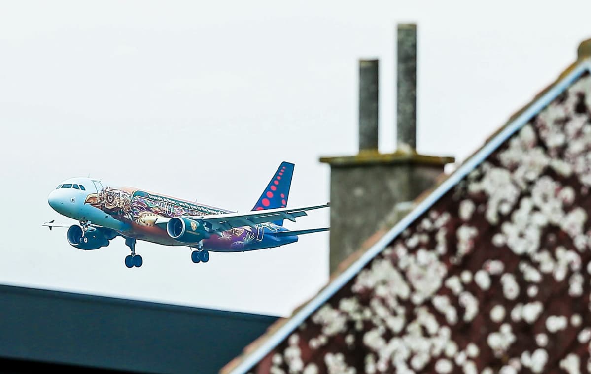 Brussels Airlinesin kone lähestyy Brysselin lentoasemaa, etualalla rakennuksen kattoa ja savupiippu.