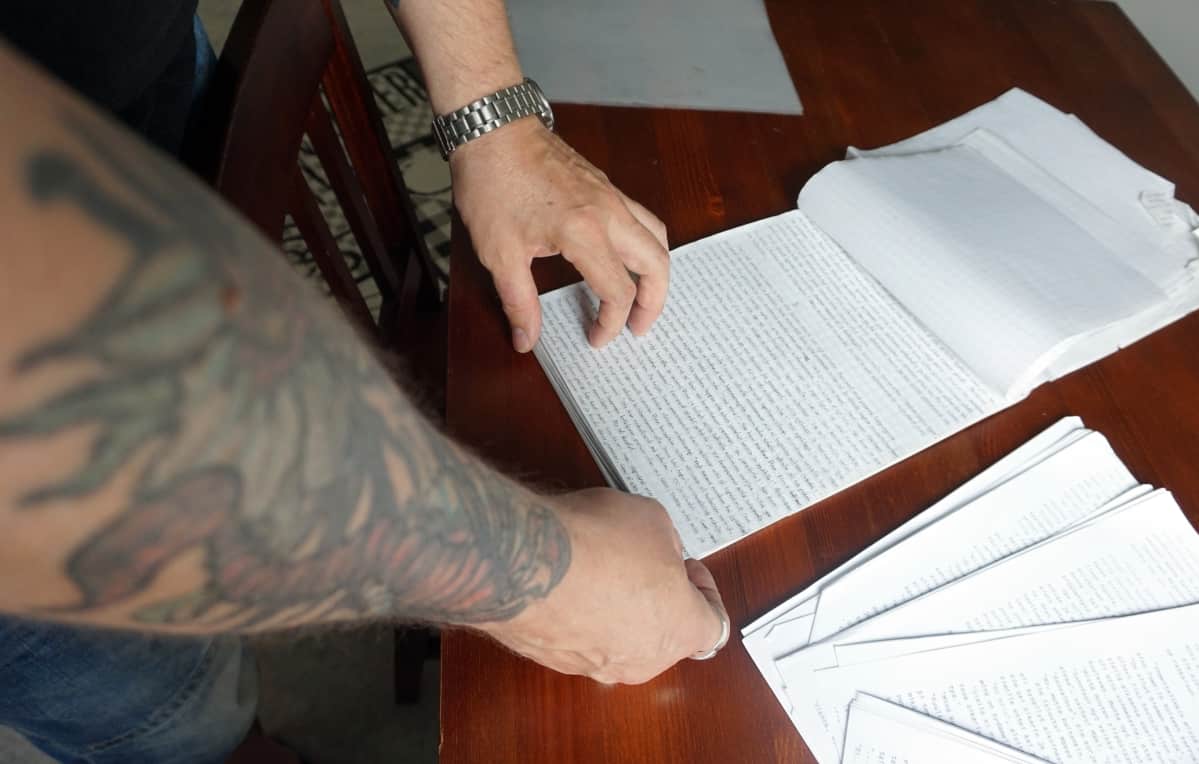 Tatuoitu käsi selaa lehtiötä