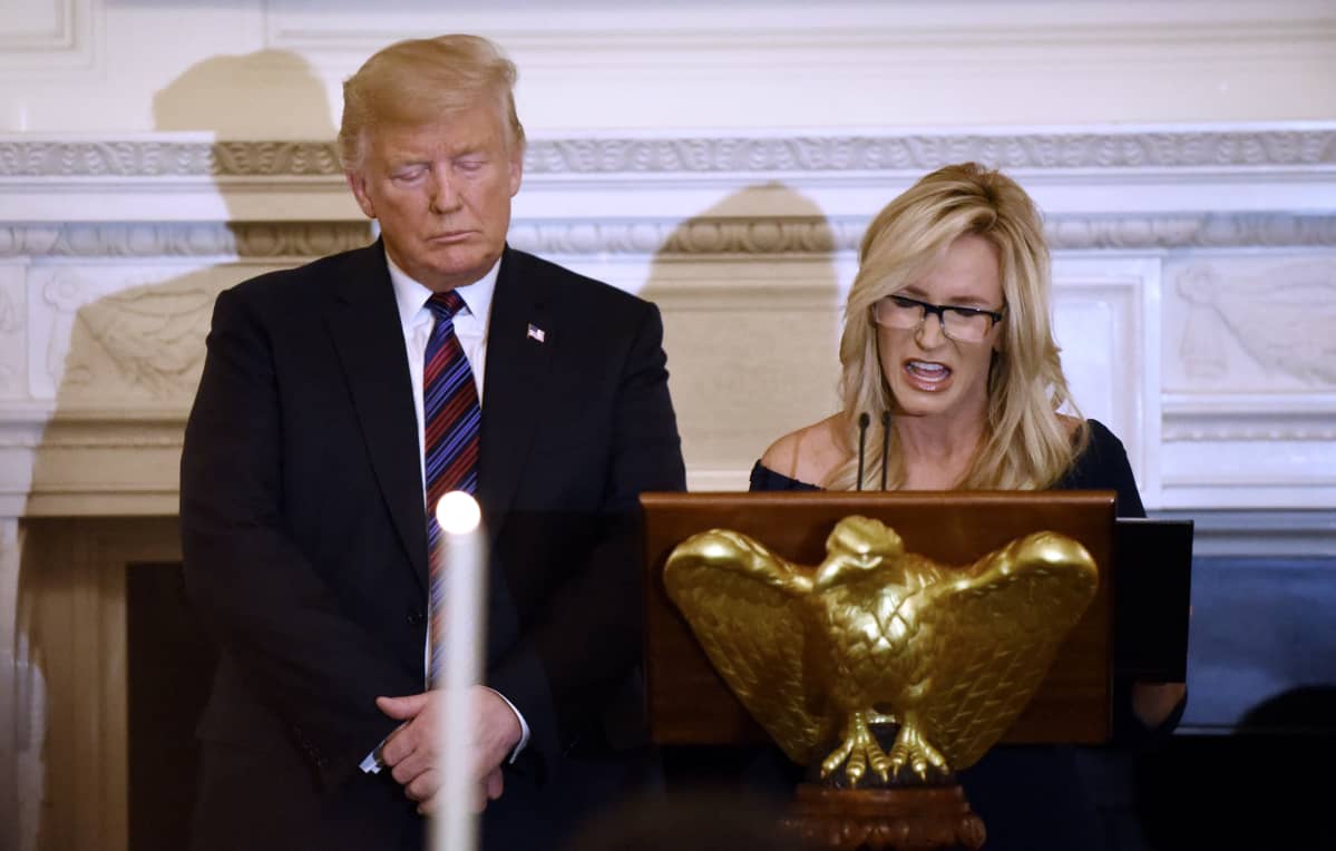 Donald Trump silmät ummessa. Vierellä Paula White, joka lukee.