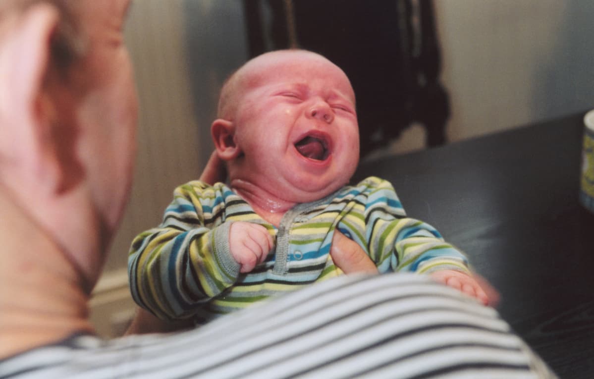 En pappa håller en fyramånaders baby som gråter.