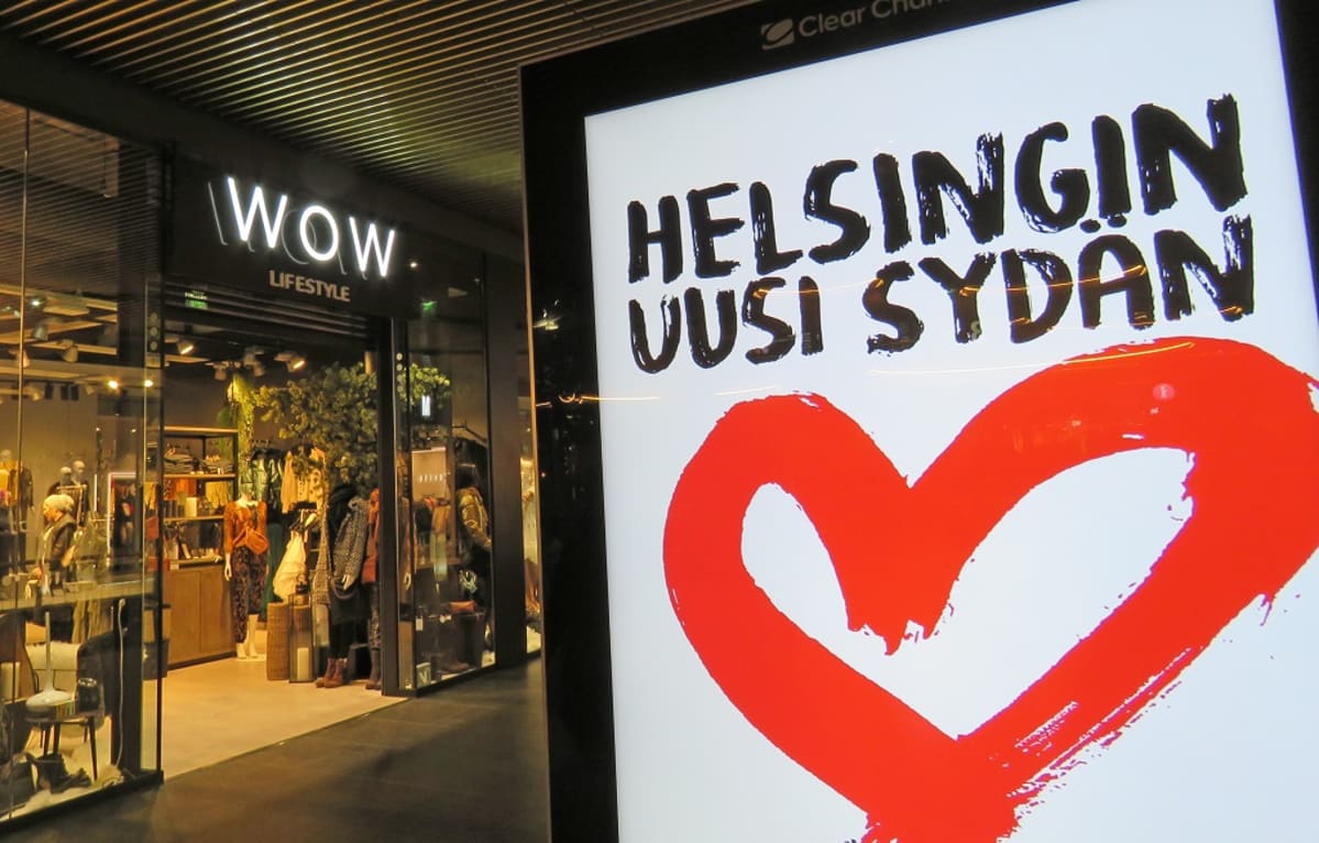 Edessä mainostaulu, jossa sydän ja teksti "Helsingin uusi sydän". Takana vaatekauppa, jonka oven päällä nimi Wow Lifestyle,